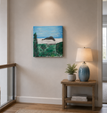 Painting of a coastal landscape on a wall above a wooden side table for upstairs hall decor.